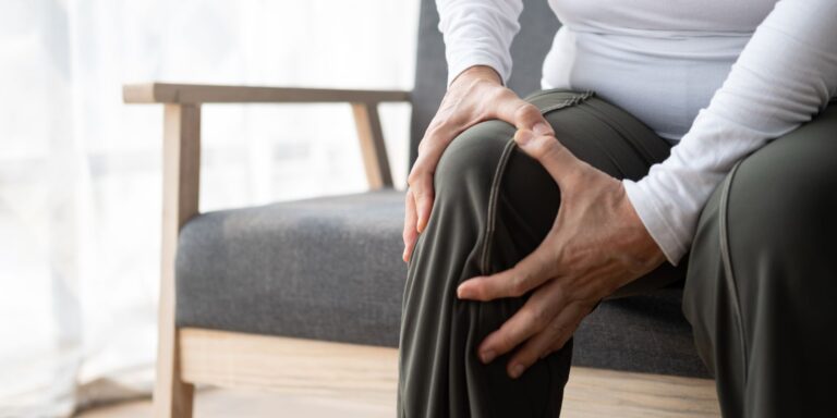 Older women sitting in a cheer holding her knee in pain