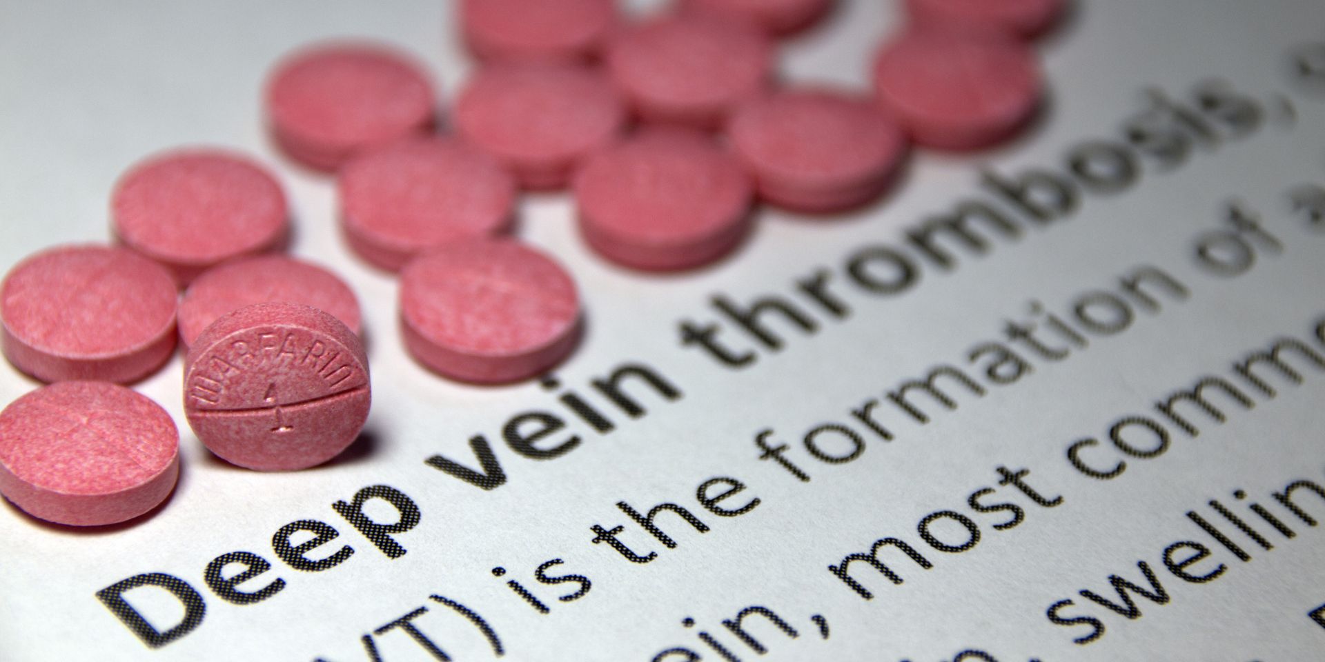warfarin pills lying above a printed definition of deep vein thrombosis