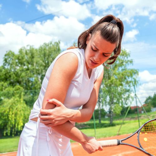 woman holding her elbow in pain during a game of tennis
