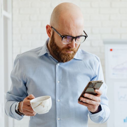 Man searching “am i at risk for vascular disease” on his phone while drinking coffee in his kitchen