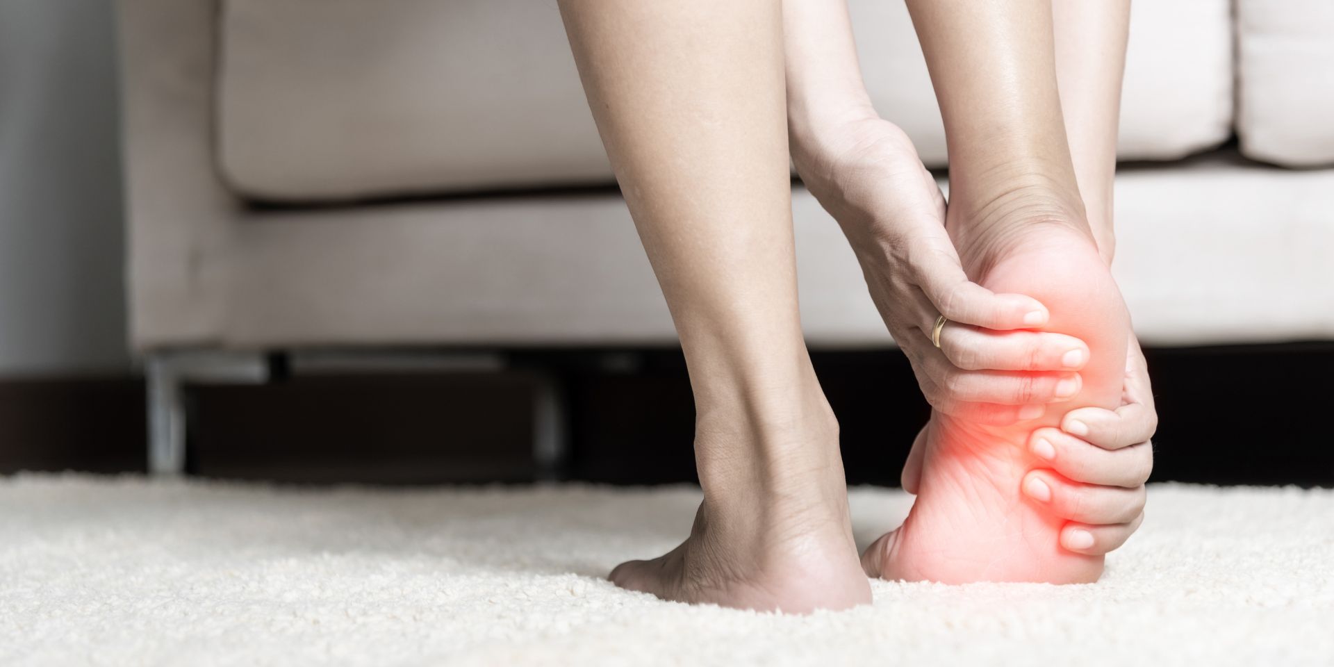 woman standing on a rug holding her foot in pain with the pained area highlighted in red